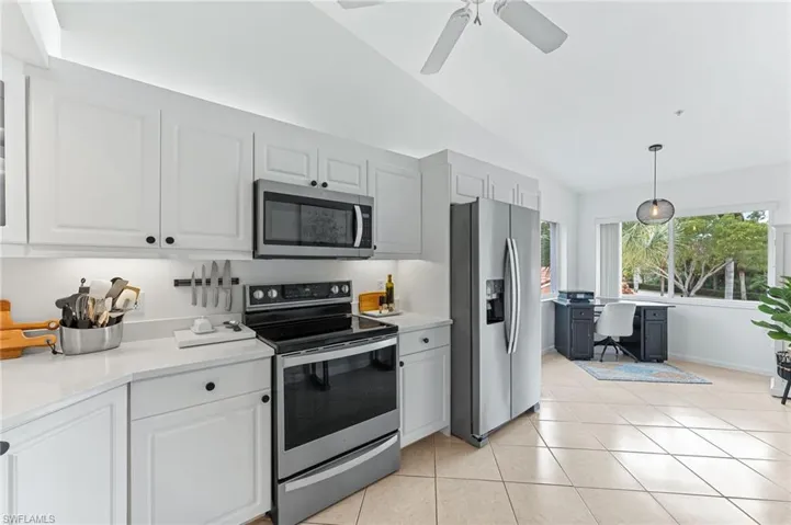 Kitchen featuring stainless steel appliances, lofted ceiling, pendant lighting, light tile patterned flooring, and a desk