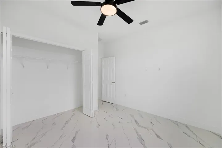 Unfurnished bedroom featuring a closet, light marble finish floors, and a ceiling fan