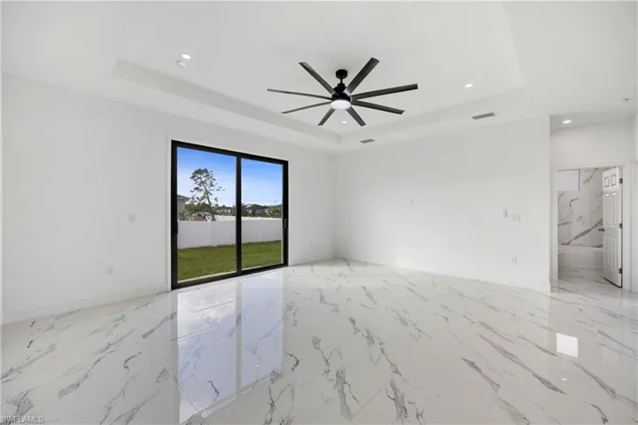 Spare room with light marble finish flooring, a tray ceiling, recessed lighting, and a ceiling fan