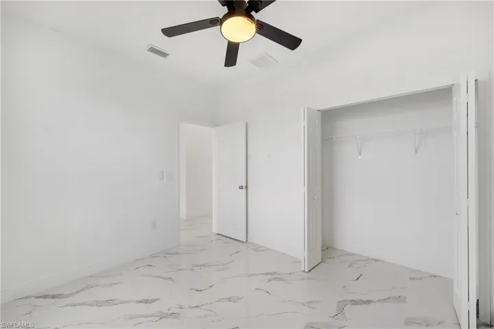 Unfurnished bedroom featuring light marble finish flooring, ceiling fan, and a closet
