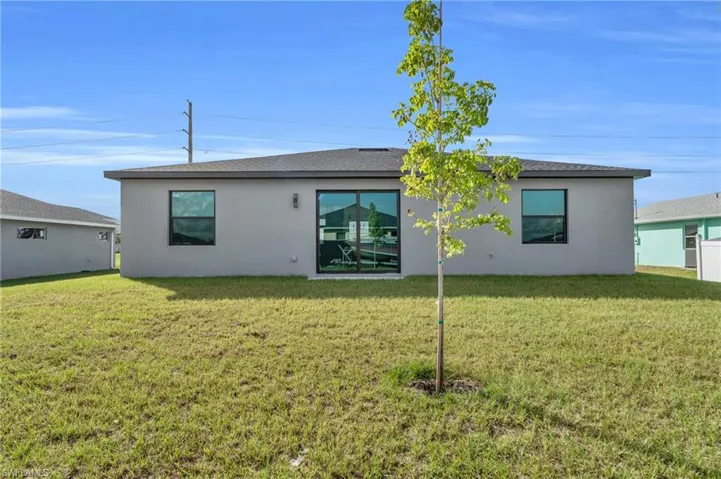 Back of property featuring a lawn, stucco siding, and roof with shingles