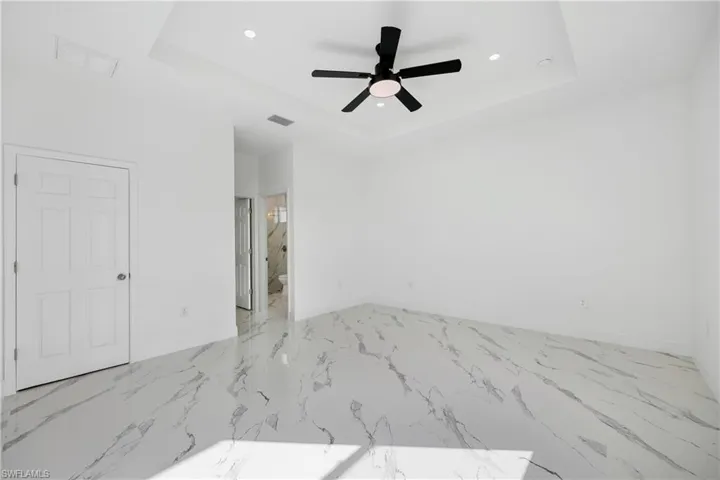 Unfurnished bedroom with a tray ceiling, recessed lighting, marble finish floors, ceiling fan, and ensuite bathroom