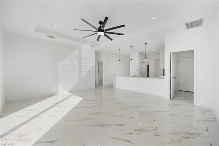 Unfurnished living room with light marble finish flooring, ceiling fan, recessed lighting, and a raised ceiling