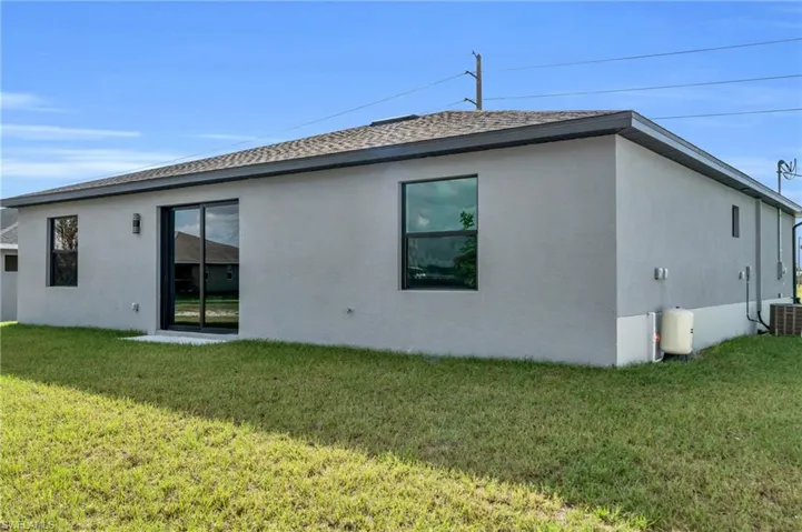 Rear view of property featuring stucco siding, a lawn, and a shingled roof