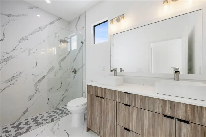 Bathroom featuring double vanity, a marble finish shower, recessed lighting, and light marble finish flooring