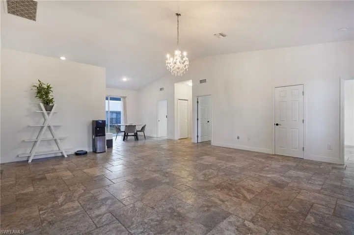 Unfurnished living room featuring a notable chandelier, visible vents, baseboards, and stone tile floors