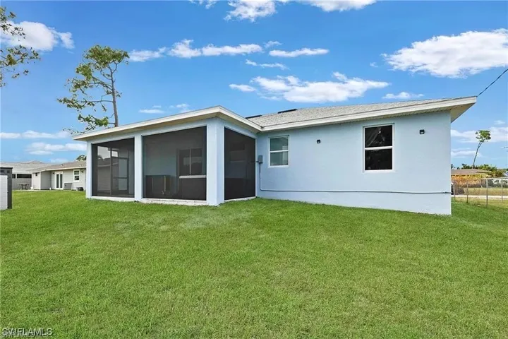 Rear view of property with fence, stucco siding, a sunroom, and a lawn