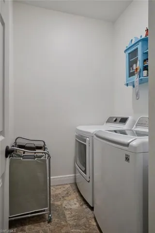 Laundry area featuring laundry area, stone finish floor, washing machine and clothes dryer, and baseboards