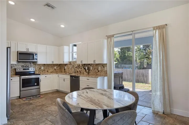 Kitchen with stainless steel appliances, a healthy amount of sunlight, stone tile flooring, and decorative backsplash