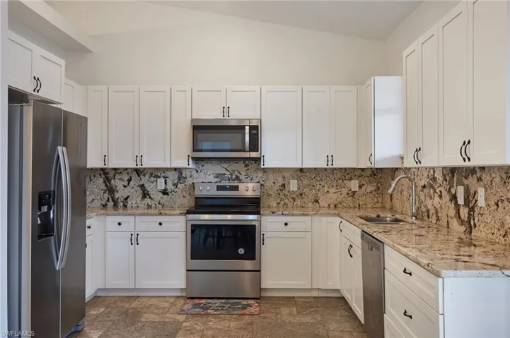 Kitchen featuring a sink, stone finish floor, white cabinetry, stainless steel appliances, and backsplash