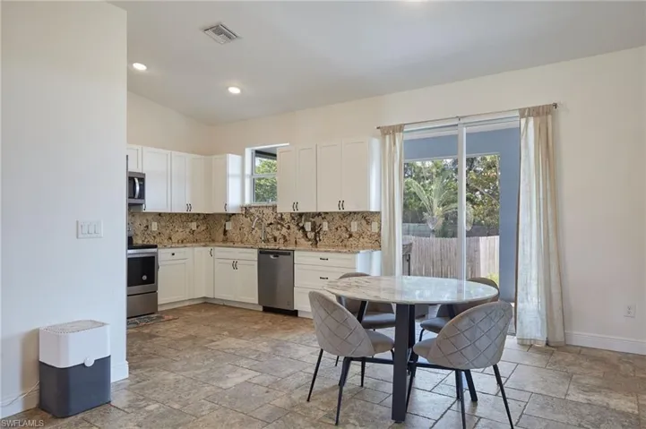 Kitchen with tasteful backsplash, appliances with stainless steel finishes, baseboards, and stone tile floors
