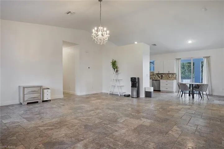 Unfurnished living room featuring visible vents, baseboards, a notable chandelier, vaulted ceiling, and stone finish flooring