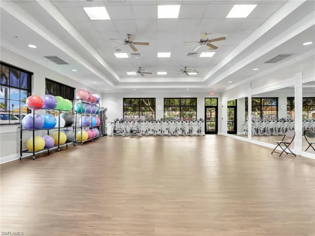 Workout room featuring wood finished floors, a raised ceiling, baseboards, and ceiling fan