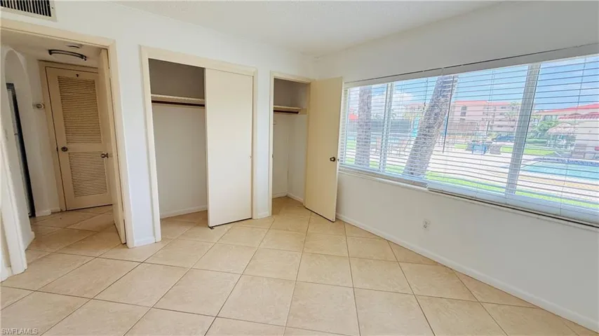 Bright room featuring tile flooring, two sliding closet doors, a solid interior door, and a large window with horizontal blinds overlooking a body of water