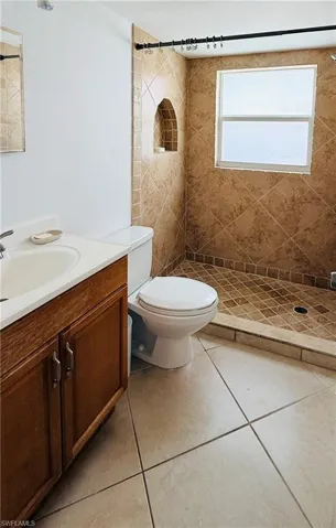 Bathroom featuring a tiled walk-in shower with an integrated niche, a window with frosted glass, and a wood-finish vanity with a white countertop