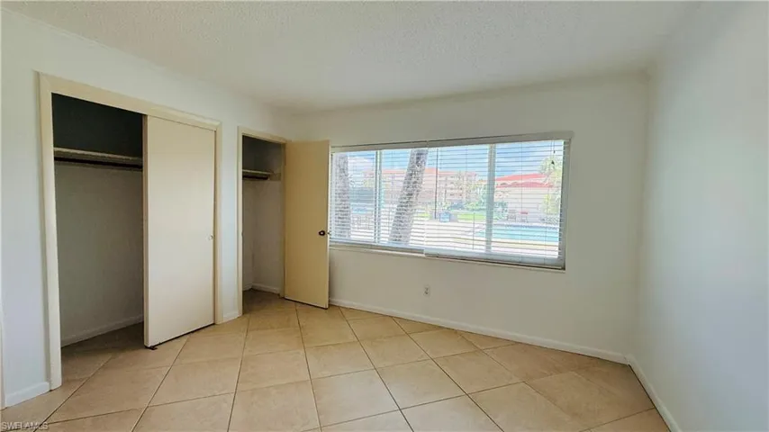 Bright room featuring tan floor tiles, a large window with horizontal blinds, and two integrated closet spaces