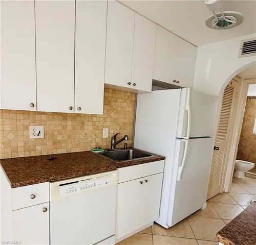 Kitchen featuring white cabinetry, a mosaic tile backsplash, a double basin sink with a chrome faucet, a white dishwasher, and a white refrigerator