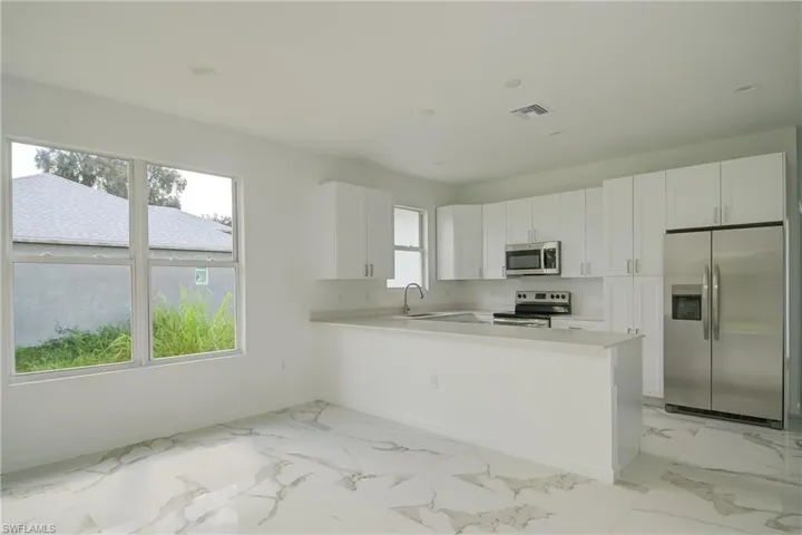 Kitchen with white cabinets, appliances with stainless steel finishes, sink, and kitchen peninsula