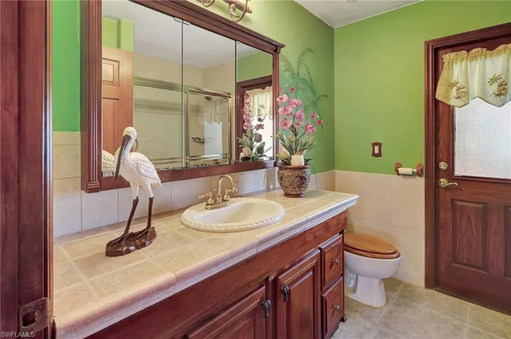 Bathroom featuring toilet, vanity, tile walls, tile patterned floors, and a shower with door