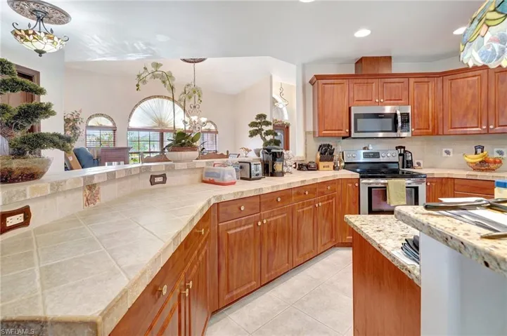 Kitchen with light tile patterned floors, stainless steel appliances, decorative backsplash, and decorative light fixtures