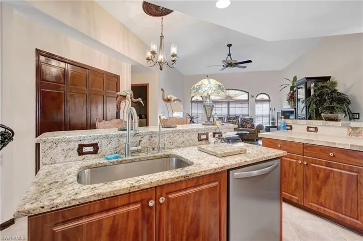 Kitchen with lofted ceiling, dishwasher, a kitchen island, sink, and ceiling fan with notable chandelier