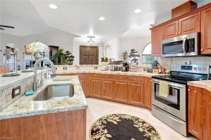 Kitchen with light tile patterned floors, stainless steel appliances, backsplash, light stone counters, and sink
