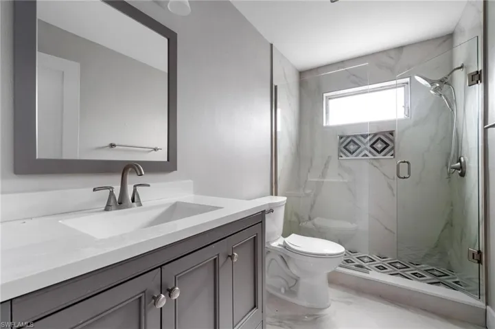 Bathroom with vanity, a marble finish shower, and marble look tiles