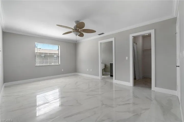 Unfurnished bedroom with a walk in closet, light marble finish floors, crown molding, a closet, and a ceiling fan