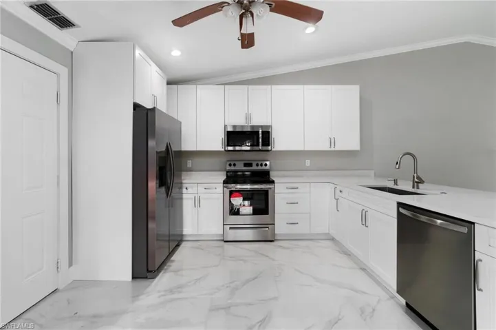 Kitchen featuring appliances with stainless steel finishes, ceiling fan, light countertops, white cabinetry, and ornamental molding