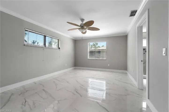 Unfurnished room featuring plenty of natural light, ornamental molding, a ceiling fan, and light marble finish floors