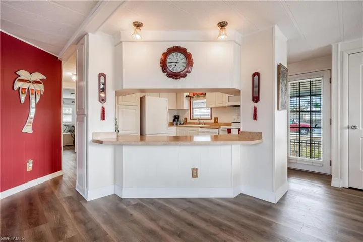 Kitchen featuring dark wood finished floors, white appliances, a peninsula, light countertops, and baseboards