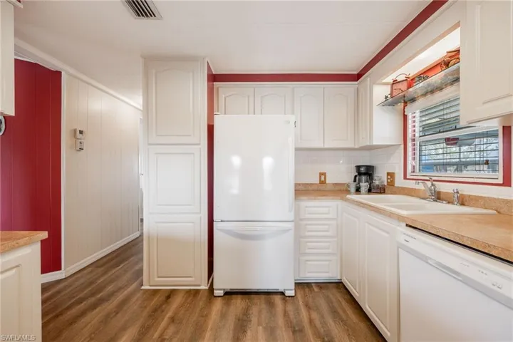 Kitchen featuring white appliances, white cabinetry, visible vents, wood finished floors, and a sink