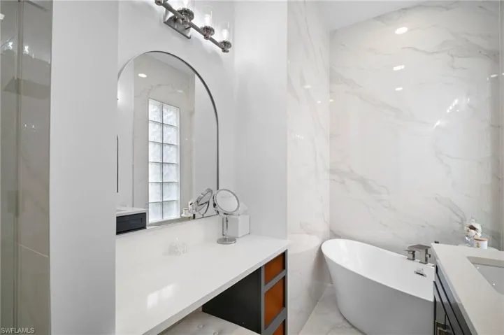 Bathroom with vanity, a freestanding tub, stone wall, light marble finish floors, and a shower with door