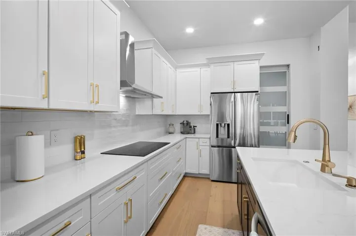 Kitchen with white cabinetry, appliances with stainless steel finishes, light wood finished floors, light stone countertops, and recessed lighting