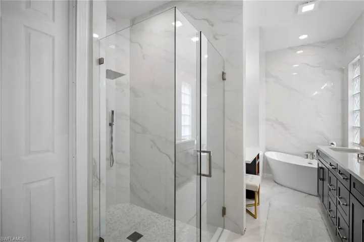Bathroom with a freestanding bath, a marble finish shower, vanity, stone wall, and tile walls