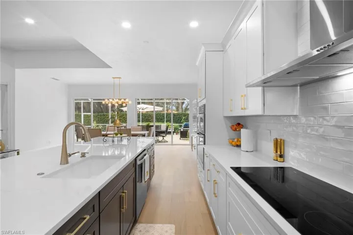 Kitchen with black electric cooktop, white cabinets, wall chimney range hood, light stone counters, and recessed lighting