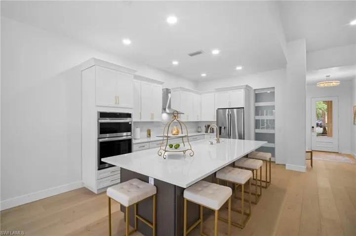 Kitchen with a kitchen breakfast bar, white cabinetry, an island with sink, light wood floors, and appliances with stainless steel finishes