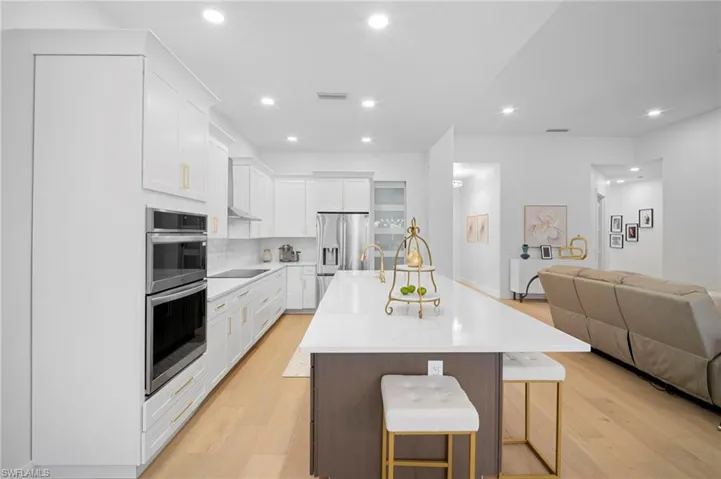Kitchen featuring white cabinets, a center island with sink, open floor plan, a kitchen breakfast bar, and light wood finished floors