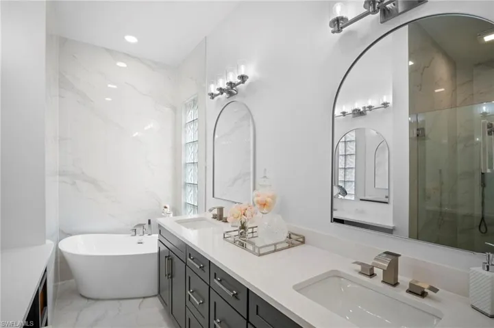 Bathroom featuring double vanity, a soaking tub, a marble finish shower, light marble finish flooring, and recessed lighting