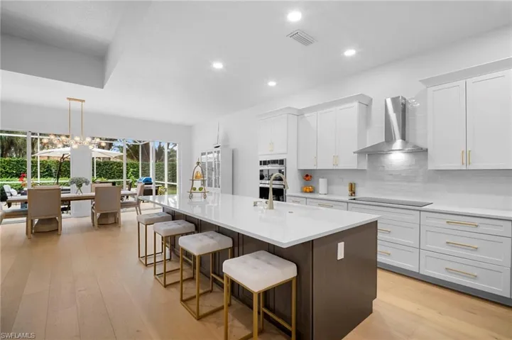 Kitchen with a breakfast bar, light wood flooring, dark brown cabinetry, wall chimney range hood, and a center island with sink