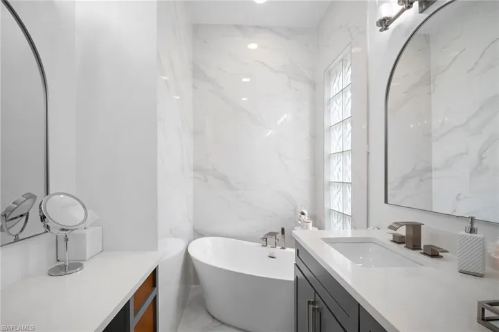 Full bathroom with vanity, a freestanding bath, light marble finish floors, stone wall, and tile walls