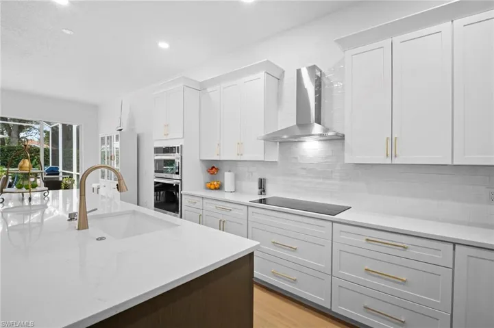 Kitchen with wall chimney exhaust hood, white cabinets, light stone counters, recessed lighting, and light wood finished floors