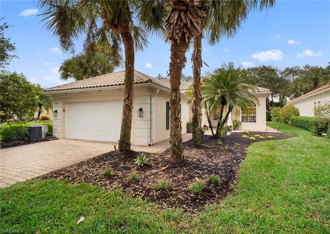 View of side of property featuring a lawn, stucco siding, a garage, decorative driveway, and a tiled roof