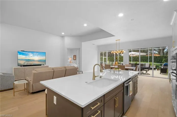 Kitchen with dark brown cabinets, open floor plan, light wood flooring, light stone countertops, and a chandelier