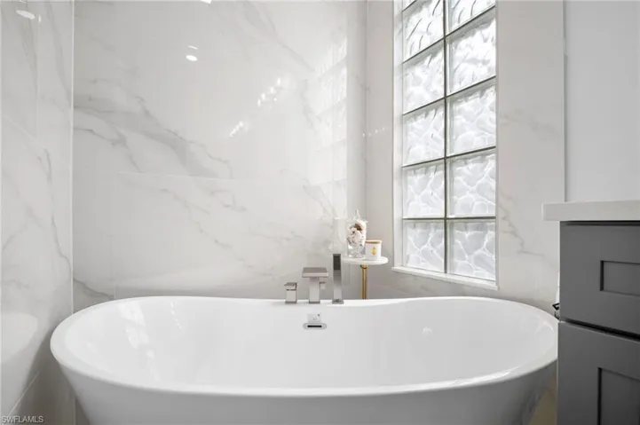 Full bath featuring a freestanding bath, stone wall, vanity, and tile walls