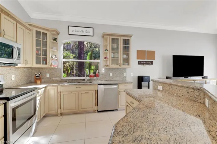 Kitchen with appliances with stainless steel finishes, glass insert cabinets, light stone counters, ornamental molding, and light tile patterned flooring