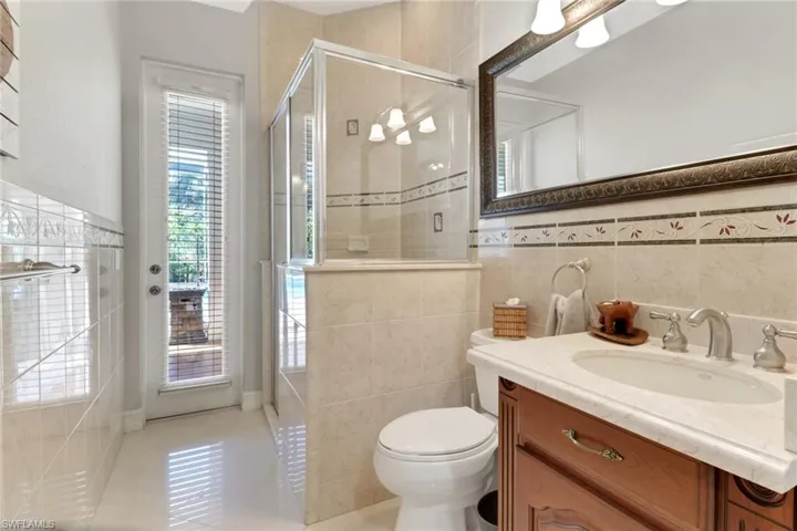 Bathroom featuring vanity, a stall shower, light tile patterned flooring, tile walls, and wainscoting