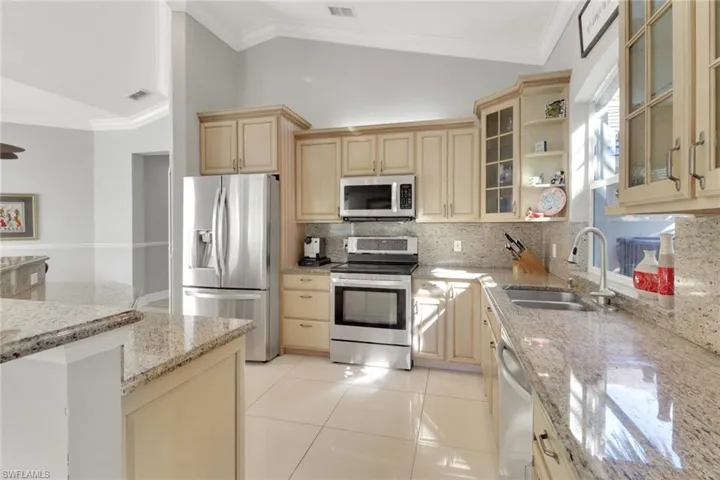 Kitchen featuring ornamental molding, open shelves, appliances with stainless steel finishes, glass insert cabinets, and vaulted ceiling