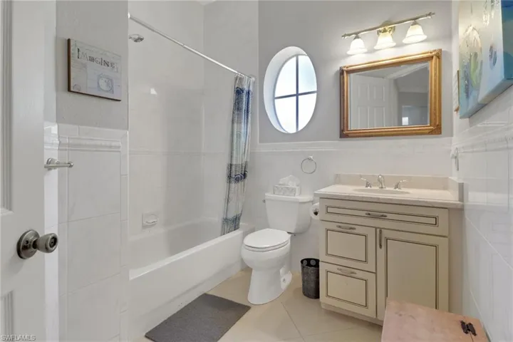 Full bath with tile walls, vanity, shower / bath combo, light tile patterned floors, and wainscoting