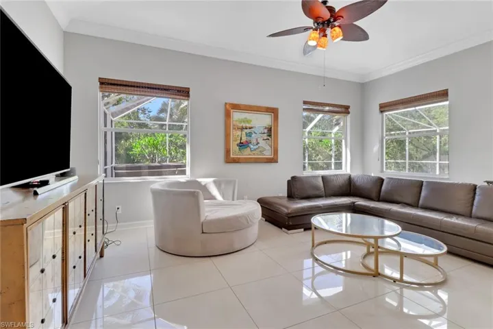Tiled living area with ornamental molding, plenty of natural light, and a ceiling fan